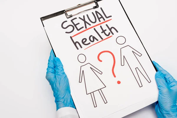 Cropped view of doctor in blue latex gloves holding clipboard with sexual health lettering, drawn man and woman isolated on white — Stock Photo