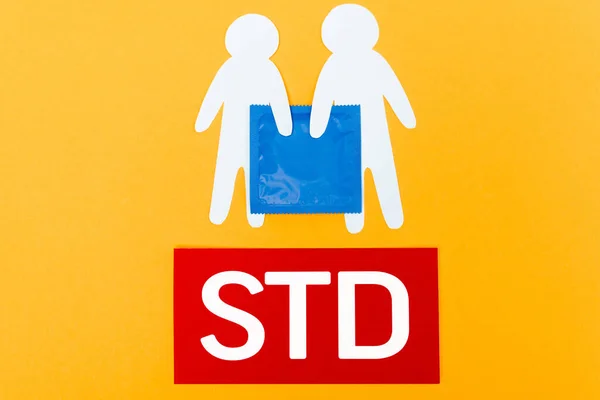 Верхний вид бумаги люди рядом с голубым презервативом и STD надписи изолированы на оранжевый — стоковое фото