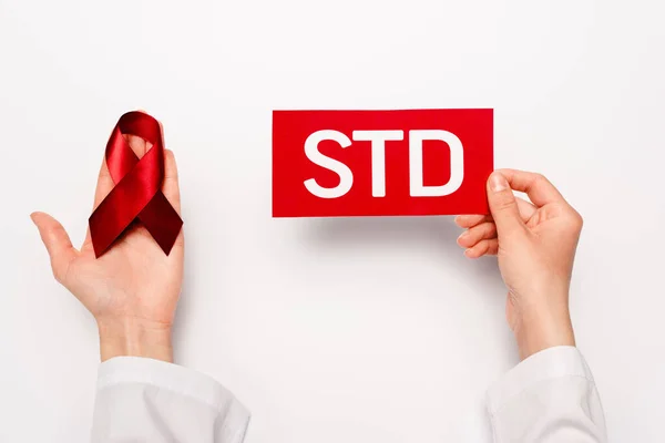 Cropped view of doctor holding paper with std lettering and red ribbon on white — Stock Photo