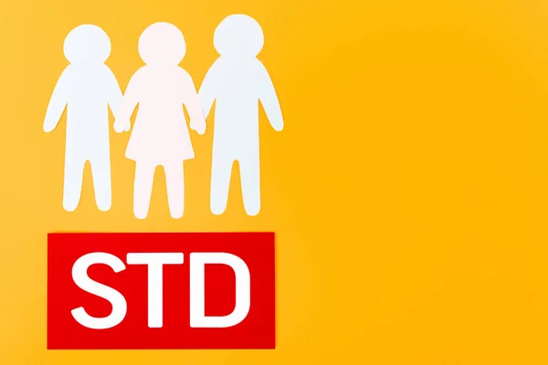 Top view of three paper people near paper with std lettering isolated on orange — Stock Photo