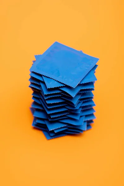 Preservativos empilhados em embalagens azuis isoladas em laranja — Fotografia de Stock
