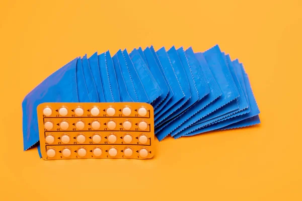 Embalagem blister com pílulas contraceptivas perto de embalagens com preservativos isolados em laranja — Fotografia de Stock