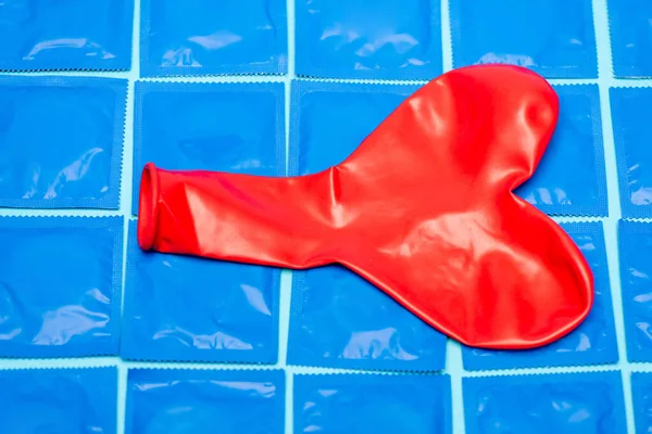Palloncino rosso a forma di cuore su confezioni con preservativi isolati su blu — Foto stock