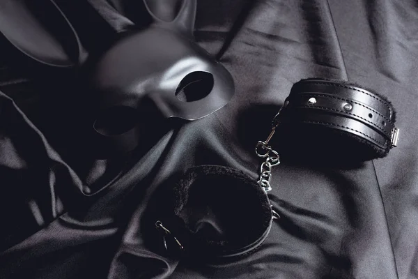 Maschera di coniglio vicino a manette in pelle su tessuto di seta nero — Foto stock