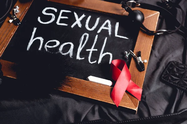 Chalkboard with sexual health lettering and sex toys and red ribbon on black silk — Stock Photo