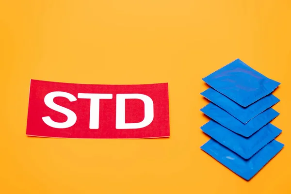Paquetes azules con condones cerca de letras std aisladas en naranja - foto de stock