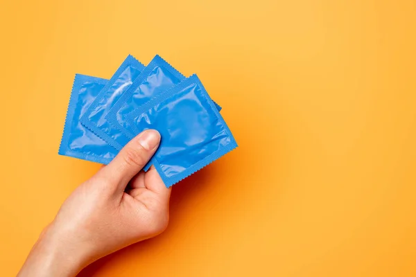 Vista recortada de la mujer sosteniendo paquetes azules con condones en naranja - foto de stock