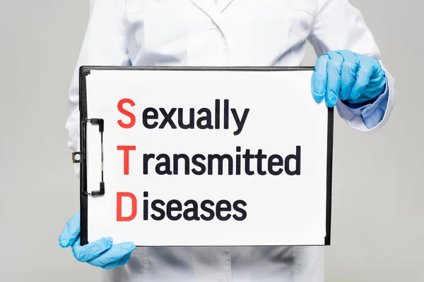 Cropped view of doctor in latex gloves holding chalkboard with sexually transmitted diseases lettering isolated on grey — Stock Photo