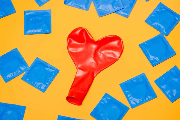 Draufsicht auf roten herzförmigen Ballon in der Nähe blauer Kondome isoliert auf orange — Stockfoto