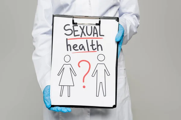 Cropped view of doctor in blue latex gloves and white coat holding clipboard with sexual health lettering, drawn man and woman isolated on grey — Stock Photo