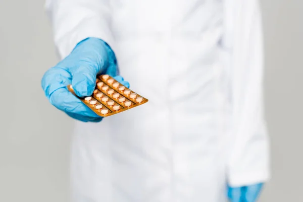 Foyer sélectif du médecin tenant une plaquette thermoformée avec des pilules contraceptives isolées sur gris — Photo de stock