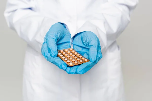 Vista recortada del médico que sostiene el blíster con píldoras anticonceptivas aisladas en gris - foto de stock