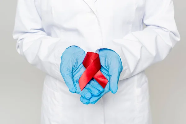 Cropped view of doctor holding red ribbon isolated on grey — Stock Photo