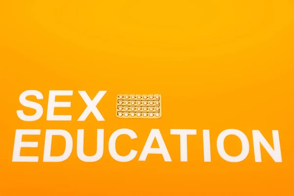 Top view of sex education lettering near blister pack with contraceptive pills isolated on orange — Stock Photo