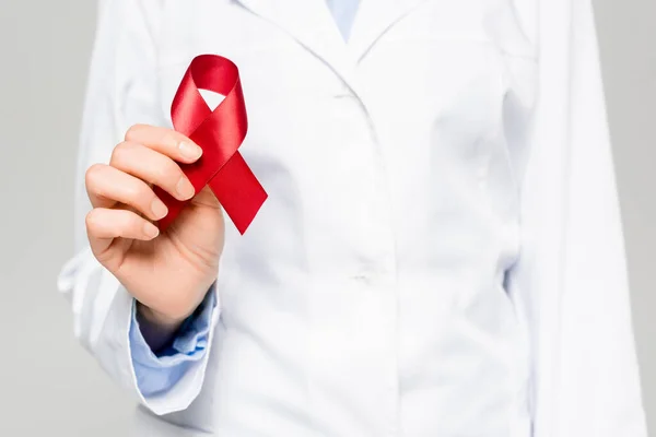 Cropped view of doctor in white coat holding red ribbon isolated on grey — Stock Photo