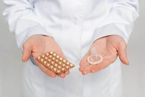 Cropped view of doctor holding blister pack with contraceptive pills and condom isolated on grey — Stock Photo