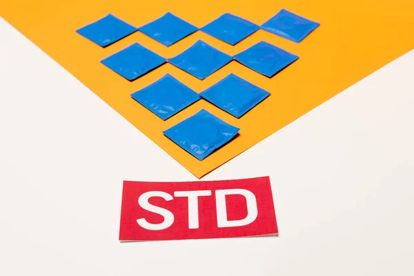 Упаковки с презервативами на оранжевой поверхности рядом с надписью STD изолированы на белом — стоковое фото