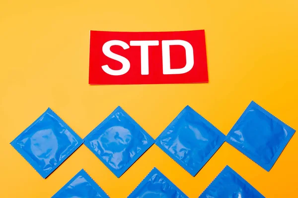 Вид сверху упаковки с презервативами рядом с красной надписью STD изолирован на оранжевом — стоковое фото