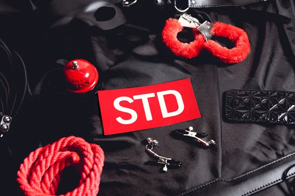 Top view of sex bell near paper with std lettering and sex toys on black — Stock Photo