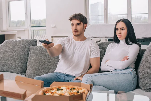 Coppia seria che mangia pizza e guarda la tv con telecomando durante l'autoisolamento a casa — Foto stock