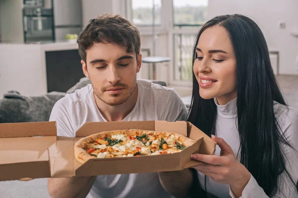 Красивая счастливая пара пахнет горячей пиццей во время самоизоляции дома — стоковое фото