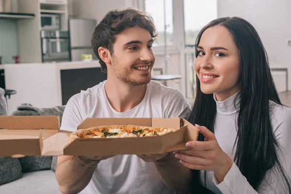 Sonriente pareja sosteniendo pizza durante auto aislamiento en casa - foto de stock