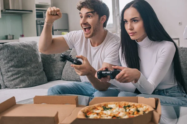 KYIV, UCRAINA - 16 APRILE 2020: coppia eccitata che mangia pizza e gioca al videogioco con i joystick durante l'autoisolamento a casa — Foto stock