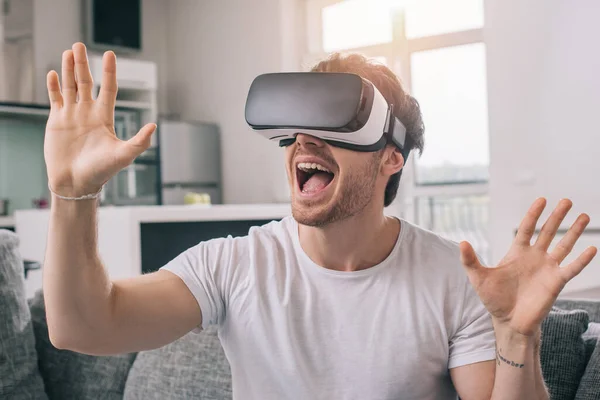 Hombre excitado usando auriculares de realidad virtual en casa en auto aislamiento - foto de stock