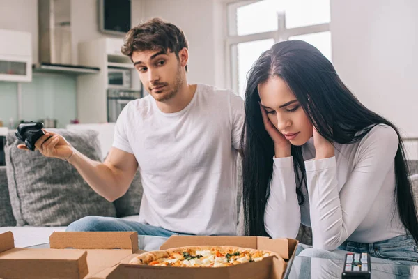 KYIV, UKRAINE - 16 de abril de 2020: jovem casal triste com pizza e joystick brigando durante o auto-isolamento em casa — Fotografia de Stock