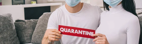 Cropped view of ill couple in medical masks holding quarantine sign at home during self isolation, horizontal concept — Stock Photo