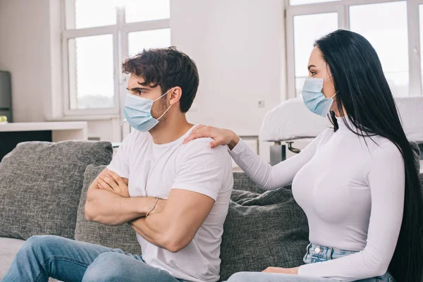 Обиженные мужчина и женщина в медицинских масках на дому во время самоизоляции — стоковое фото