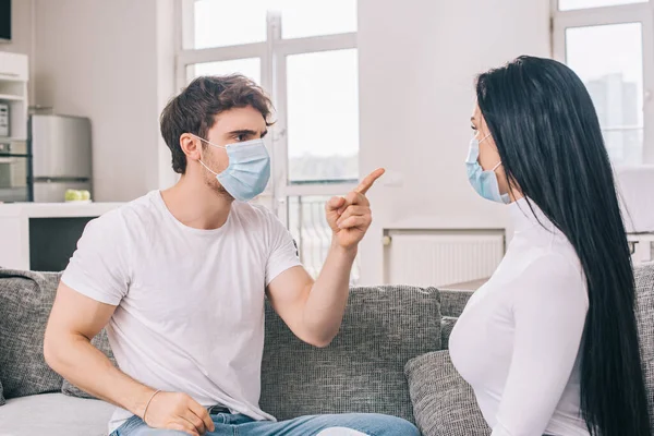 Молодая пара в медицинских масках ссорящаяся дома во время самоизоляции — стоковое фото