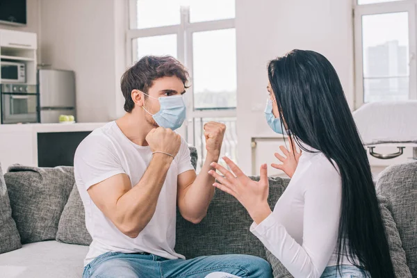 Couple malade dans des masques médicaux gesticuler et se quereller à la maison pendant l'isolement personnel — Photo de stock