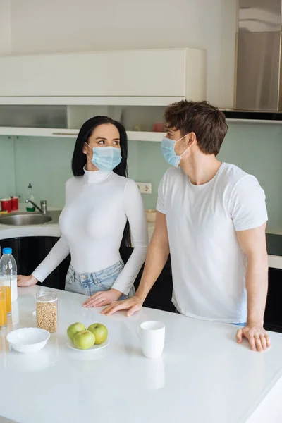 Beau couple dans des masques médicaux prendre le petit déjeuner à la maison pendant l'isolement personnel — Photo de stock