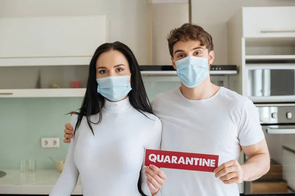 Couple malade dans des masques médicaux tenant signe de quarantaine à la maison pendant l'isolement personnel — Photo de stock