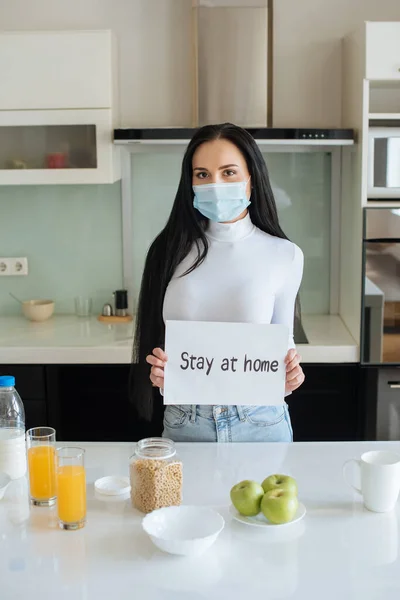 Ill woman in medical mask holding Stay at home sign during breakfast at home on self isolation — Stock Photo