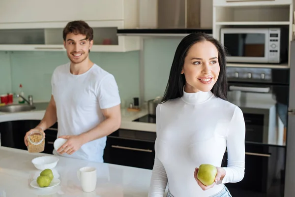 Веселая пара с кукурузными хлопьями и яблоками на завтрак во время самоизоляции дома — стоковое фото
