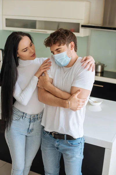 Beautiful girl hugging cold ill boyfriend in medical mask at home during self isolation — Stock Photo