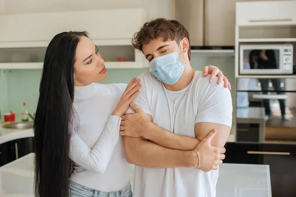 Mulher abraçando homem doente frio em máscara médica em casa durante o auto-isolamento — Fotografia de Stock