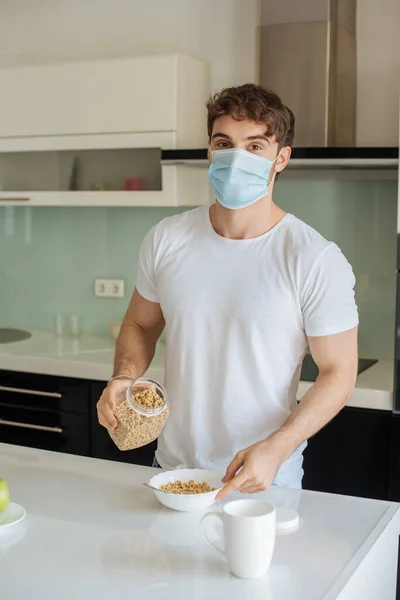 Больной человек в медицинской маске делает кукурузные хлопья на завтрак на кухне по самоизоляции — стоковое фото