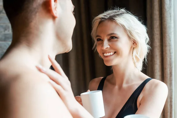 Selective focus of smiling girl touching boyfriend neck while holding mug — Stock Photo
