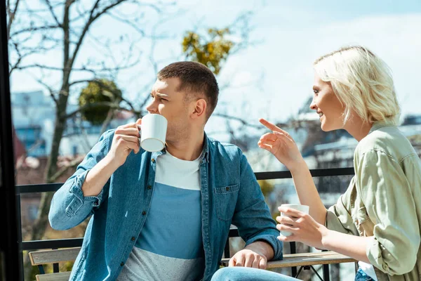 Smiling couple talking and drinking tea on terrace while woman pointing with finger away — Stock Photo