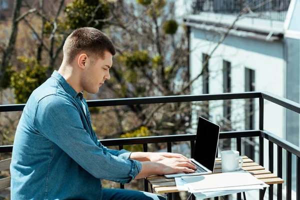 Freelancer sentado en terraza con laptop y papeles - foto de stock