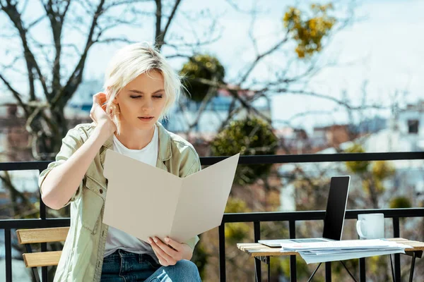 Freelancer sitting on terrace with folder near laptop, drink and papers — Stock Photo