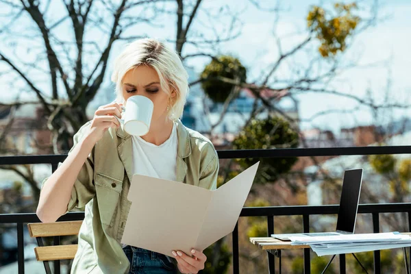 Freelancer sitting on terrace with folder near laptop and drinking tea — Stock Photo