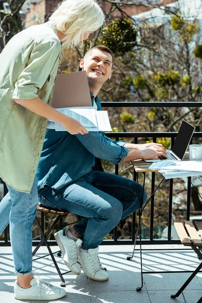 Smiling business people working with laptop and papers on sunny terrace — Stock Photo