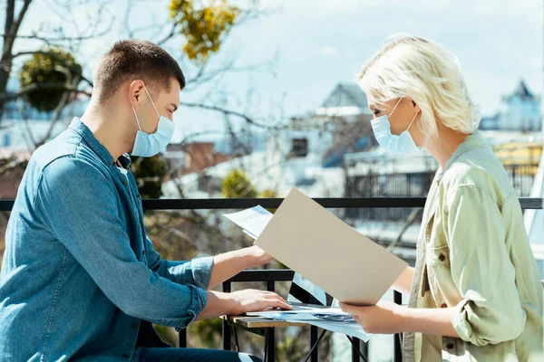 Geschäftsleute in medizinischen Masken arbeiten mit Laptop und Papieren auf sonniger Terrasse — Stockfoto