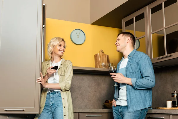 Улыбающаяся пара пьет красное вино вместе на кухне — стоковое фото