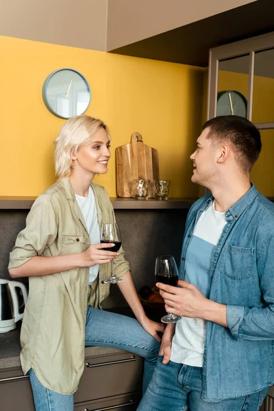 Улыбающаяся пара пьет красное вино вместе на кухне — стоковое фото