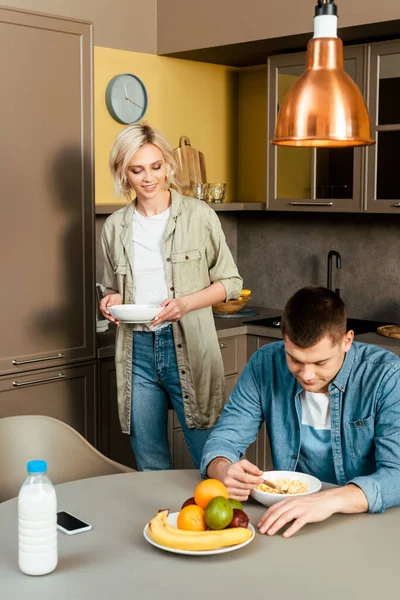 Улыбающаяся пара завтракает с хлопьями и фруктами на кухне — стоковое фото